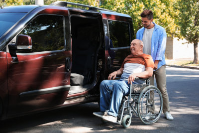 caregiver helping an elderly man get into the van